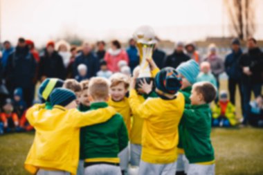 Blurred Background of Kids Sport Team with Trophy. Kids Celebrating Football Championship. Happy Young Soccer Players Holding Golden Cup. Football Team Winning Youth Soccer Tournament  clipart