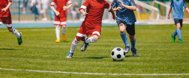 Futbol futbol oyuncu topu ile çalışan. Futbolcular futbol maçı tekme. Genç futbol oyuncular topun peşinde koşuyoruz. Çocuklar futbol kırmızı ve mavi üniforma. Futbol Stadyumu içinde belgili tanımlık geçmiş 