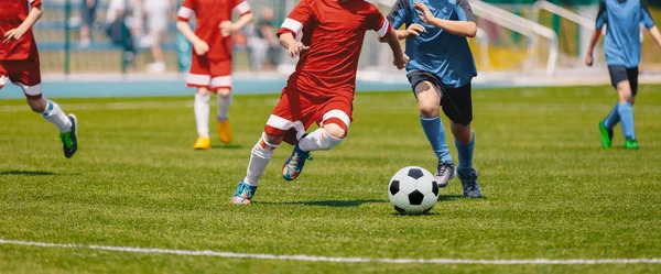 サッカー サッカー選手がボールを実行しています サッカーの試合を蹴る選手 若いサッカー選手がボールを追いかけてします 子供サッカー赤と青のユニフォーム バック グラウンドでサッカー スタジアム — ストック写真