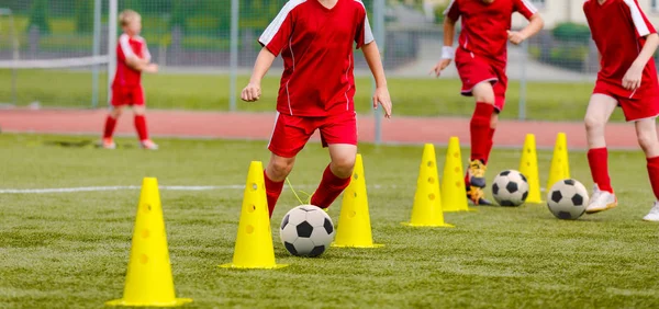 Soccer camp for kids. Boys practice dribbling in a field. Players develop good soccer dribbling skills. Children training with balls and cones. Soccer slalom drills to improve football dribbling pace