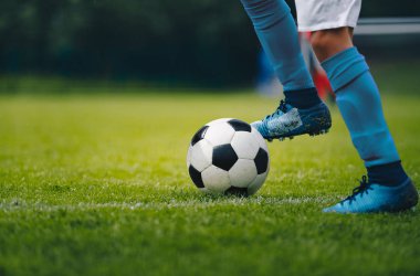 Mavi çorap ve ayakkabı çalışan ve topla top sürme futbolcunun bacak ve ayakları kapatın. Futbol oyuncusu topun peşinden koşuyor. Arka planda spor salonu