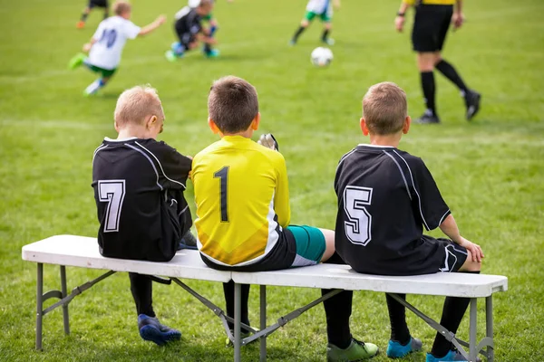 Voetbal Bench. Jonge voetballers zittend op voetbal vervangende Bank. Voetbalwedstrijd en scheidsrechter op de achtergrond — Stockfoto