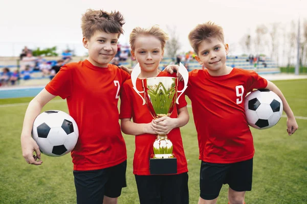 stock image Three Happy Cheerful Kids of Sports Soccer Team. Boys Football Players Holding Trophy at the Stadium. Young Winners of Youth Football Tournament