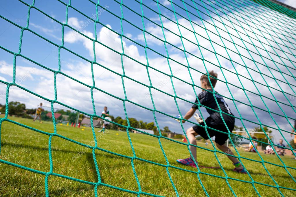Soccer goal with a young boy goalkeeper. Youth football goalkeeper save. Soccer goalkeeper at saving penalties. View from behind the goal nets. Football goalkeeping background