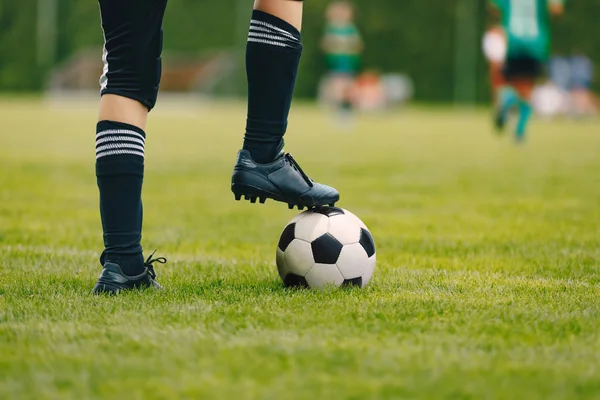 Un joven futbolista con pelota en el campo de hierba. Un chico con ropa deportiva. Jugador con calcetines de fútbol negro y zapatos de fútbol. Fútbol horizontal primer plano fondo —  Fotos de Stock