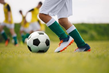 Detaylı futbolcu sahada topa vuruyor. Futbol oyuncuları antrenman yapıyor. Futbol geçmişini detaylandır. Yeşil çimenlikteki futbolcunun bacaklarına ve ayaklarına yakın dur.