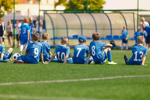 ユースサッカーチームのメンバーが一緒にフィールドに座っている 子供たちはサッカートーナメントゲームをプレイ ブルースポーツユニフォームの子供たち — ストック写真