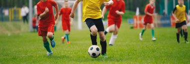 Futbolcular Koşar. Futbol Turnuvası Maçı sırasında top peşinde koşan genç çocuklar. Çocuklar için Spor Okulu Yarışması. Küçükler düzeyinde futbol maçı. Kırmızı ve Sarı Jersey Spor Giyim Oyuncuları. 