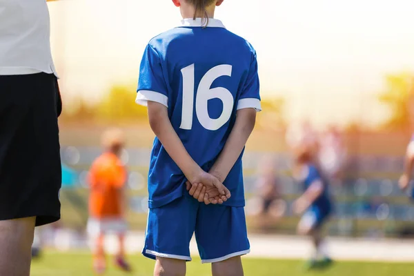 Soccer Boy in Blue Uniform on The Field. School Kid Standing with Coach. Youth Sports Competition in the Blurred Background
