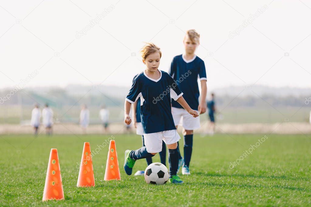 Boys training unit on soccer field. Young footballers practice dribbling skills on the grass pitch. Kids running between red soccer training cones. Summer soccer camp for children team