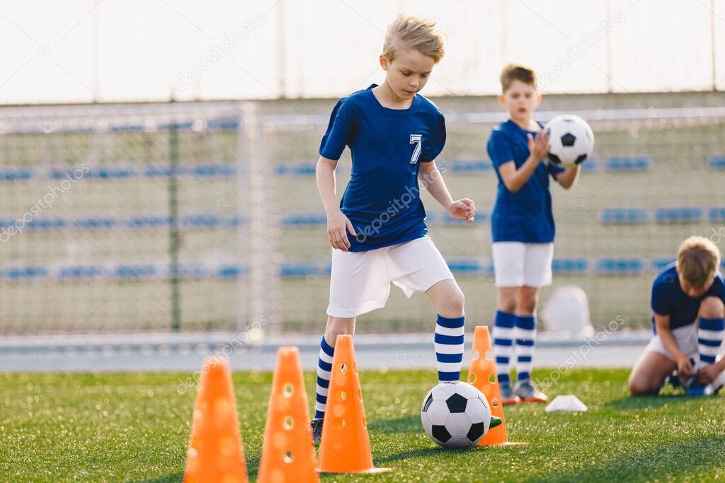 Young boys kicking soccer ball on training. Children practicing football on school grass pitch. Happy blonde boy running after soccer ball and training dribbling skills between cones