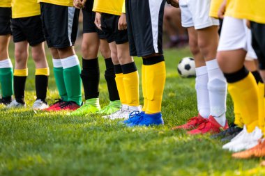 Futbol antrenmanındaki çocuklar. Futbolcular arka arkaya diziliyor. Spor giyim ve krampon giymiş futbolcu bacaklarının düşük açılı görüntüsü. Renkli futbol kıyafeti
