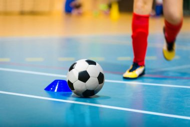 Futbol topu, ahşap zemin, antrenman işareti ve kramponlu koşucu. Kapalı spor salonu. Futsal spor geçmişi. Kapalı Futbol Kış Ligi