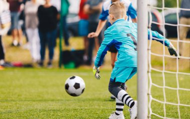 Erkek futbol kalecisi iş başında. Genç futbolcu futbol topuna doğru koşuyor. Çocuk Kaleci Futbol Okul Turnuvasında Tasarruf
