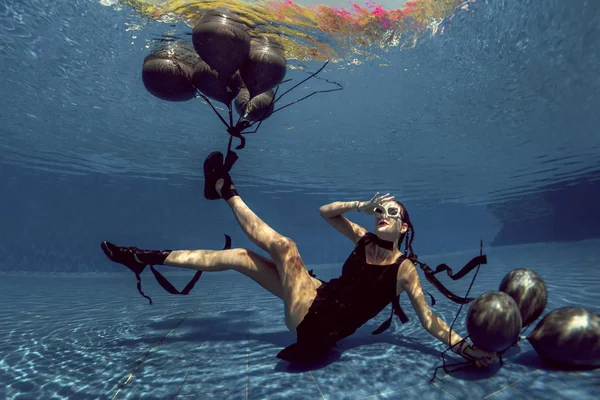 Underwater shoot of flying woman with black balloons