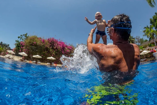 Funny photo of  happy active family young father with active baby diving in swimming pool with fun jump .