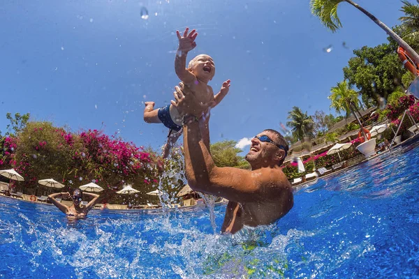 Funny photo of  happy active family young mother with active baby diving in swimming pool with fun jump .