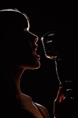 Siluet siyah arka plan üzerinde mikrofon önünde şarkıcı