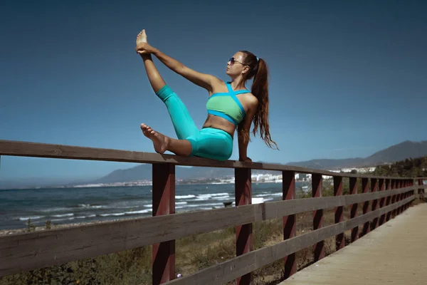 side view of woman practicing yoga and stretching leg near sea during summer vacation in Spain