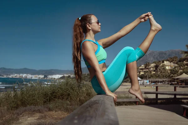 在西班牙暑假期间练习瑜伽和在海边伸展腿的妇女的侧视图 — 图库照片