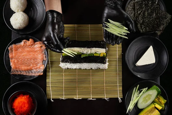 制作加州卷寿司的过程是在黑色背景的黑色手套中 用鲑鱼 奶油芝士 红玛瑙鱼子酱等配料制成的 — 图库照片
