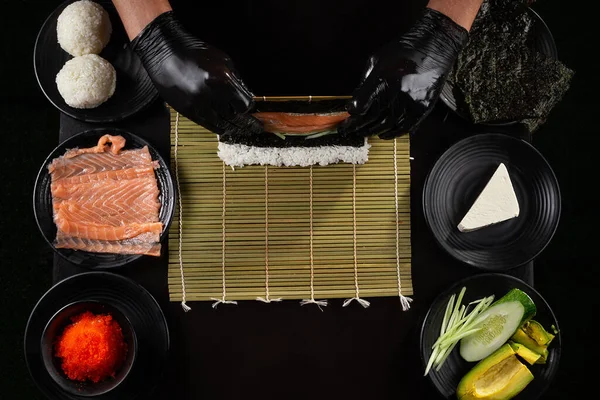 制作加州卷寿司的过程是在黑色背景的黑色手套中 用鲑鱼 奶油芝士 红玛瑙鱼子酱等配料制成的 — 图库照片