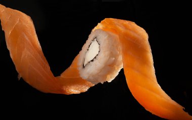 Somon filetosu spiral şeklinde siyah arka planda Philadelphia peynirli suşi rulosunu sarar.