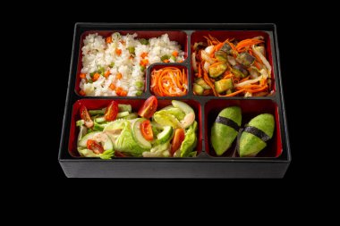 Vejetaryen Bento öğle yemeği: Taze salatalı avokado suşisi, soğanlı patlıcan yahnisi ve siyah arka planda sebzeli pilav.