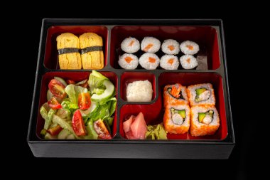 Bento öğle yemeği, Shaki maki, Uramaki suşi, Tamago sushi taze salata, Japon usulü zencefil ve siyah arka planda wasabi.