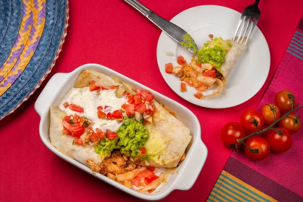 メキシコ料理 南アメリカ料理 トウモロコシ グアカモーレ トマト チリとスパイシーな鶏のエンチラーダの伝統的な料理 ベーキングトレイの上にあり その一部はプレート上にあり 複数の色のテーブルクロスの背景にあります トップ表示 — ストック写真