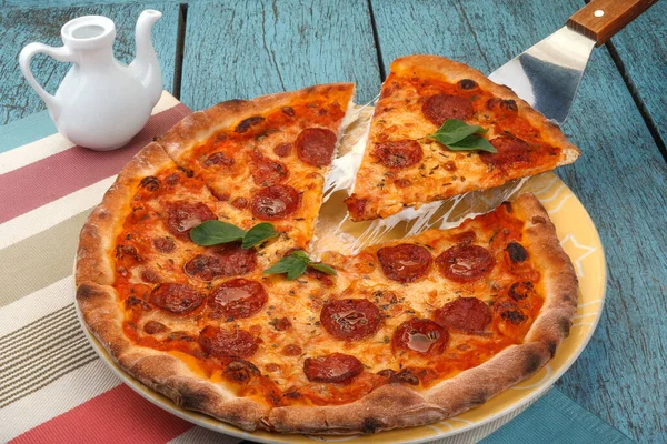 Delicious cheese stringy slice lifted of Freshly Baked Homemade Pepperoni Pizza with basil leaves on a wooden table. Fast Food concept