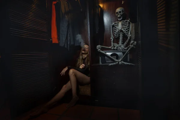 A young woman is smoking with a skeleton in a cupboard. Many people cannot part with their ghosts.
