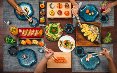 Japon mutfağından hoşlanan dört kişinin manzarası çeşitli mezeler ve kokteyller. Philadelphia, Tuna uramaki, Çiçekli suşi seti, Gyoza, Fırında misket tüfeği, ton balığı, onigiri suşi seti ve inari suşi seti.