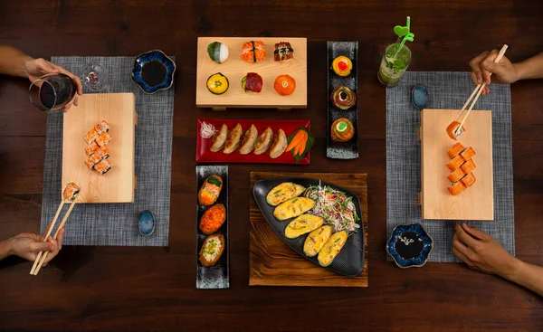 Elevated view of couple enjoying Japanese cuisine various side dishes by chopstick. Philadelphia, Tuna uramaki, Flower sush set, Gyoza, Baked mussles, tuna uramaki, onigiri sushi set and inari sushi set