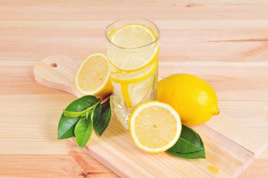 Limonlu bir bardak limonata ve ahşap arka planda yeşil yapraklar..