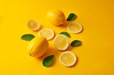 Limonlar ve yeşil yapraklar parlak sarı arka planda. Yemek konsepti, düz konum. Limon meyvesi, narenciye minimum konsept, C vitamini limon ve yapraktan yapılmış yaratıcı arka plan..