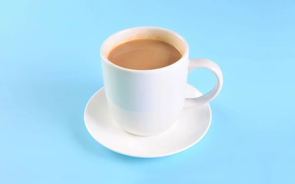 White cup of creamy coffee isolated on blue background.