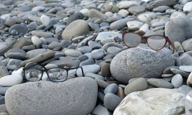 Sahilde unutulmuş, yuvarlak taşların üzerinde duran eski gözlükler.