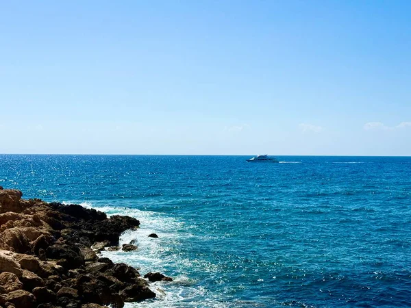 Resimli plaj, kumlu kıyıya vuran dalgalar. Deniz dalgaları kayalara çarpıyor. Kıbrıs adası, şemsiyeler, turist botları, Akdeniz.