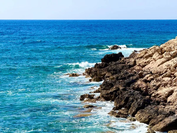 Resimli plaj, kumlu kıyıya vuran dalgalar. Deniz dalgaları kayalara çarpıyor. Kıbrıs adası, şemsiyeler, turist botları, Akdeniz.