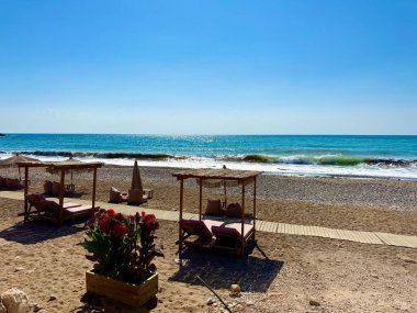 Halk plajı, yaz mevsimi, güzel güneşli hava. Resimli plaj, kumlu kıyıya vuran dalgalar. Deniz dalgaları kayalara çarpıyor. Kıbrıs adası, şemsiyeler, turist botları, Akdeniz.