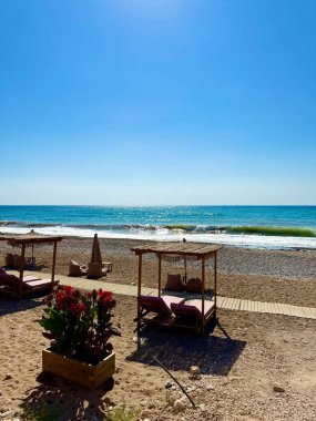 Halk plajı, yaz mevsimi, güzel güneşli hava. Resimli plaj, kumlu kıyıya vuran dalgalar. Deniz dalgaları kayalara çarpıyor. Kıbrıs adası, şemsiyeler, turist botları, Akdeniz.