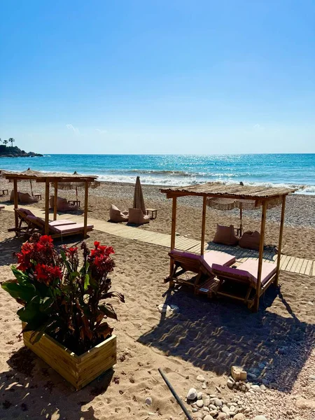 Halk plajı, yaz mevsimi, güzel güneşli hava. Resimli plaj, kumlu kıyıya vuran dalgalar. Deniz dalgaları kayalara çarpıyor. Kıbrıs adası, şemsiyeler, turist botları, Akdeniz.