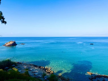 Halk plajı, yaz mevsimi, güzel güneşli hava. Resimli plaj, kumlu kıyıya vuran dalgalar. Deniz dalgaları kayalara çarpıyor. Kıbrıs adası, şemsiyeler, turist botları, Akdeniz.