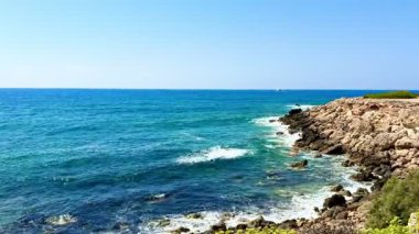 Halk plajı, yaz mevsimi, güzel güneşli hava. Resimli plaj, kumlu kıyıya vuran dalgalar. Deniz dalgaları kayalara çarpıyor. Kıbrıs adası, şemsiyeler, turist botları, Akdeniz.