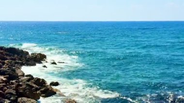 Halk plajı, yaz mevsimi, güzel güneşli hava. Resimli plaj, kumlu kıyıya vuran dalgalar. Deniz dalgaları kayalara çarpıyor. Kıbrıs adası, şemsiyeler, turist botları, Akdeniz.