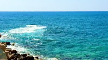 Halk plajı, yaz mevsimi, güzel güneşli hava. Resimli plaj, kumlu kıyıya vuran dalgalar. Deniz dalgaları kayalara çarpıyor. Kıbrıs adası, şemsiyeler, turist botları, Akdeniz.