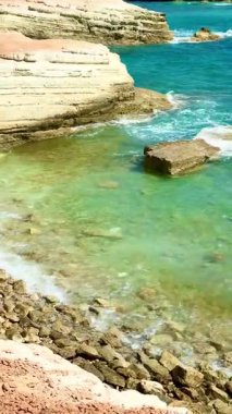 Halk plajı, yaz mevsimi, güzel güneşli hava. Resimli plaj, kumlu kıyıya vuran dalgalar. Deniz dalgaları kayalara çarpıyor. Kıbrıs adası, şemsiyeler, turist botları, Akdeniz.