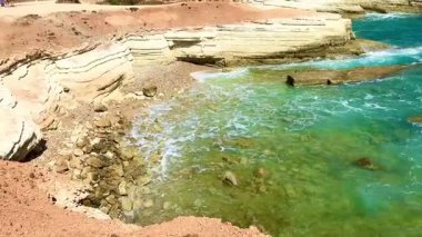 Halk plajı, yaz mevsimi, güzel güneşli hava. Resimli plaj, kumlu kıyıya vuran dalgalar. Deniz dalgaları kayalara çarpıyor. Kıbrıs adası, şemsiyeler, turist botları, Akdeniz.