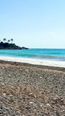 Halk plajı, yaz mevsimi, güzel güneşli hava. Resimli plaj, kumlu kıyıya vuran dalgalar. Deniz dalgaları kayalara çarpıyor. Kıbrıs adası, şemsiyeler, turist botları, Akdeniz.